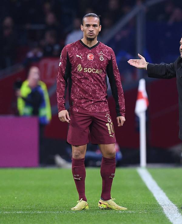 Leroy Sané steht an der Seitenlinie, neben ihm gestikuliert Trainer Okan Buruk.