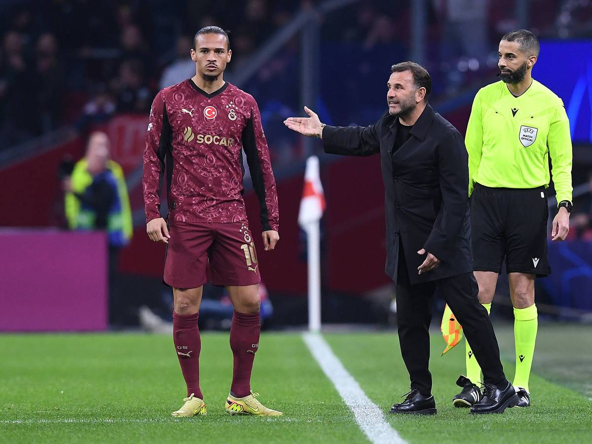 Leroy Sané steht an der Seitenlinie, neben ihm gestikuliert Trainer Okan Buruk.