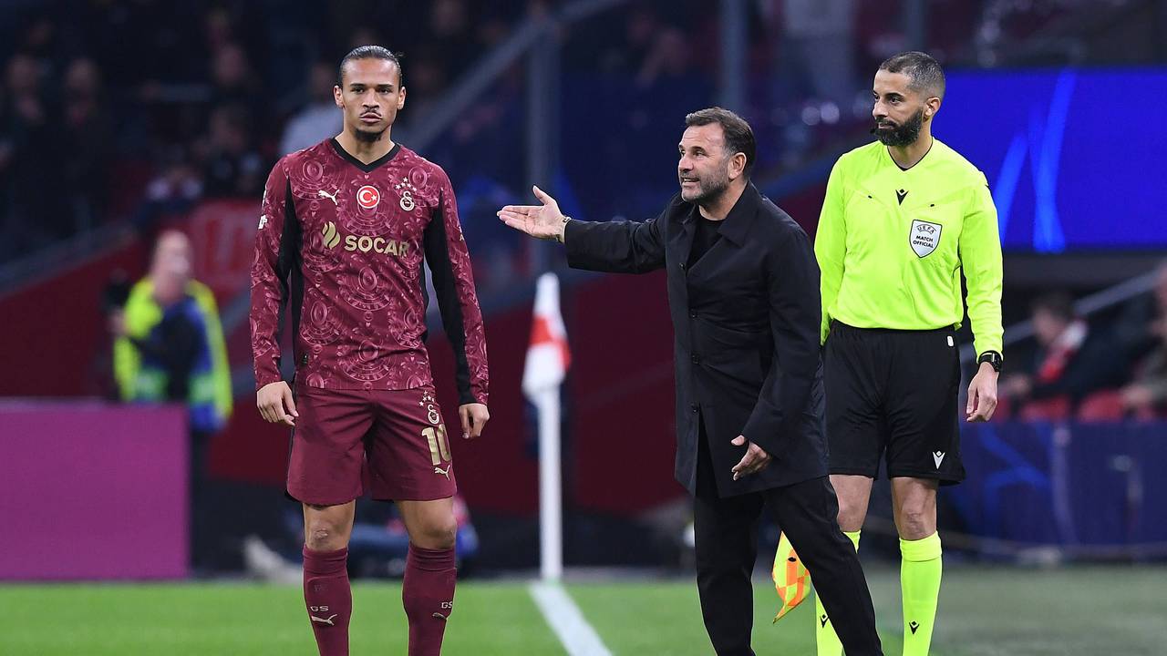 Leroy Sané steht an der Seitenlinie, neben ihm gestikuliert Trainer Okan Buruk.