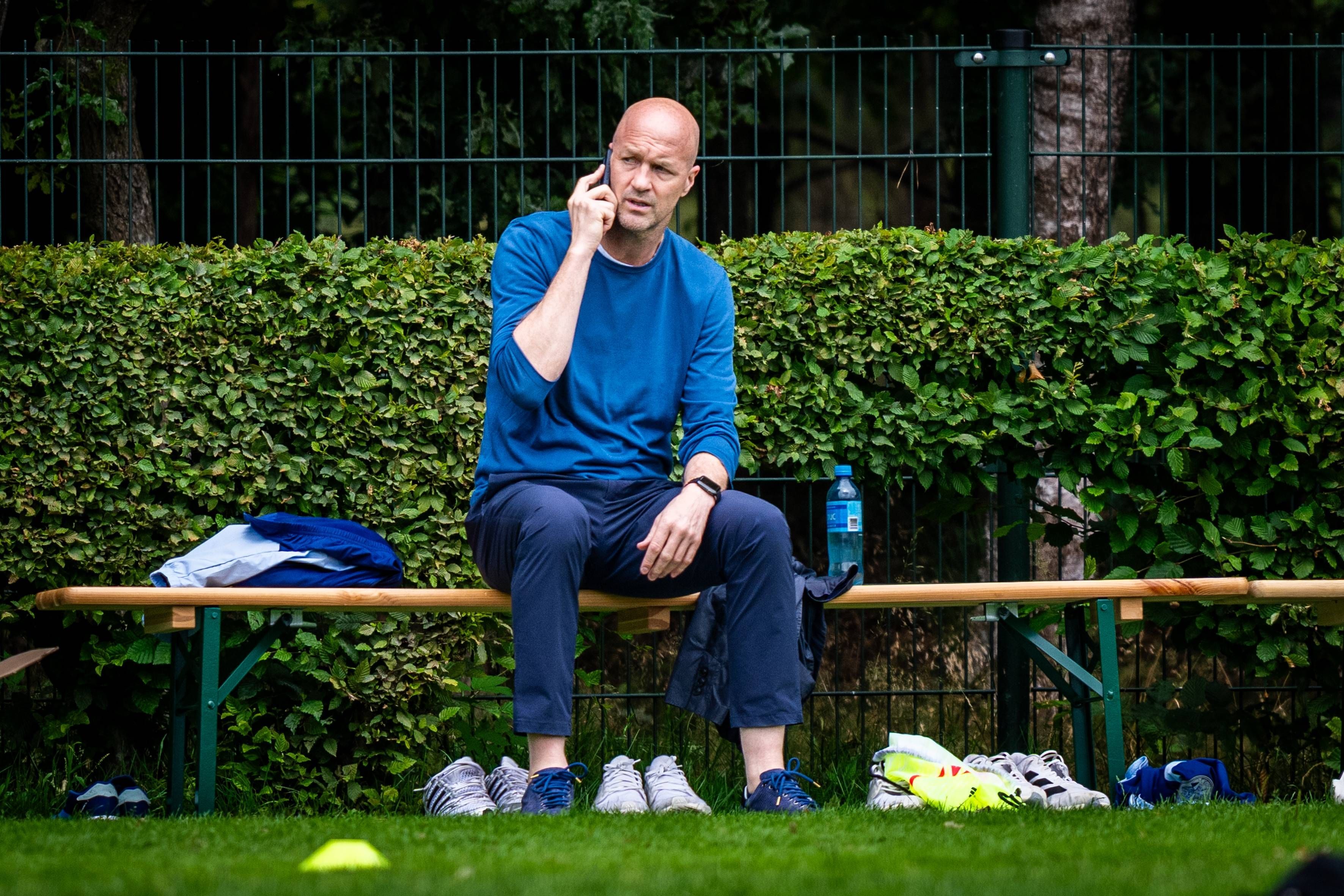 Am Rande des Trainings von Ajax Amsterdam telefoniert Jordy Cruyff auf einer Bierbank sitzend.