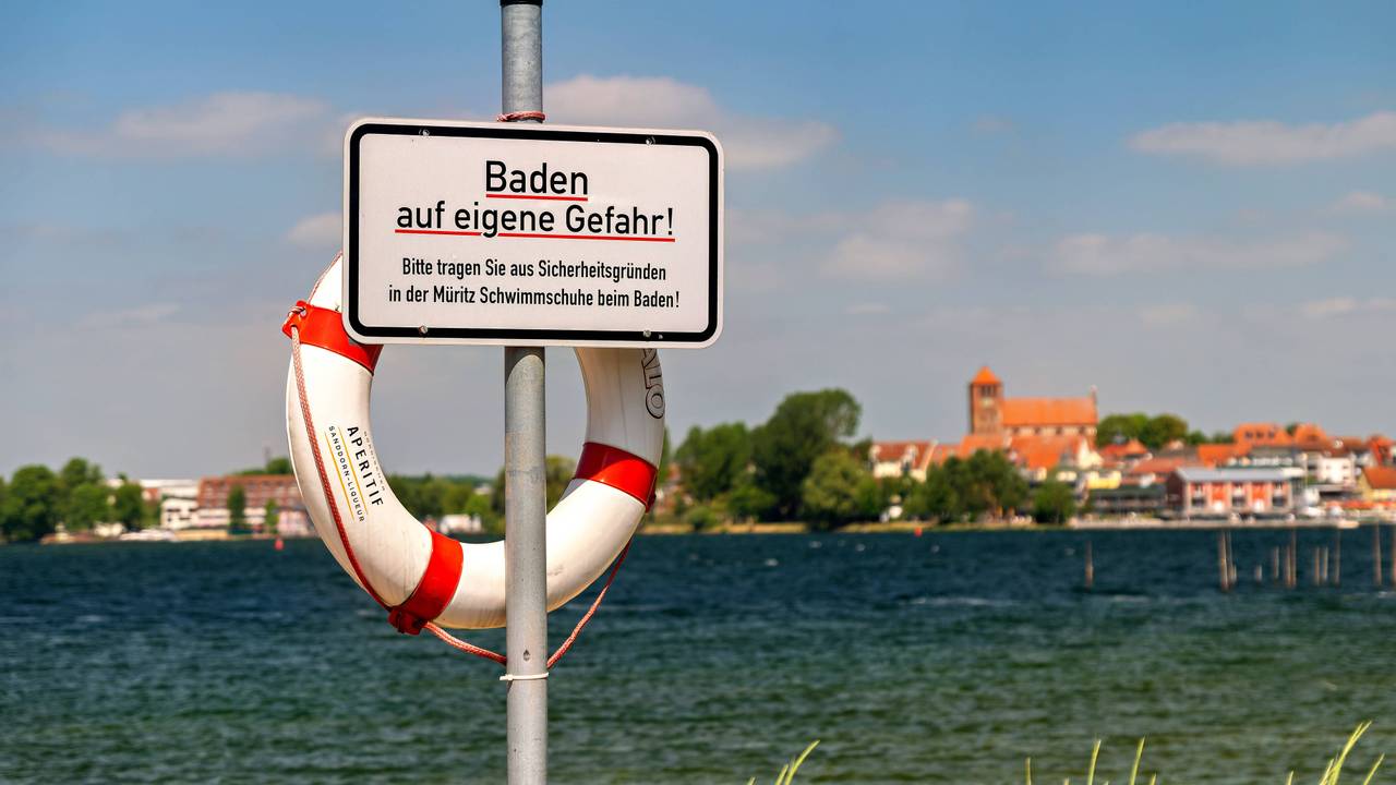 Ein Blick auf Waren Müritz in Mecklenburg-Vorpommern im Landkreis Mecklenburgische Seenplatte. m Vordergrund steht ein Schild mit dem Aufdruck „Baden auf eigene Gefahr“.