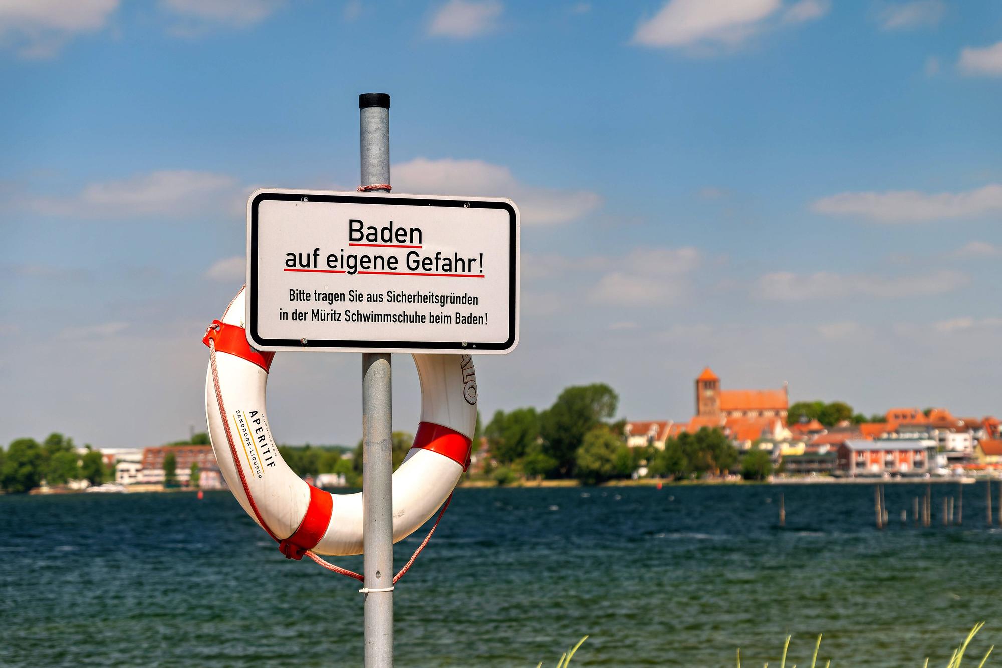 Ein Blick auf Waren Müritz in Mecklenburg-Vorpommern im Landkreis Mecklenburgische Seenplatte. m Vordergrund steht ein Schild mit dem Aufdruck „Baden auf eigene Gefahr“.