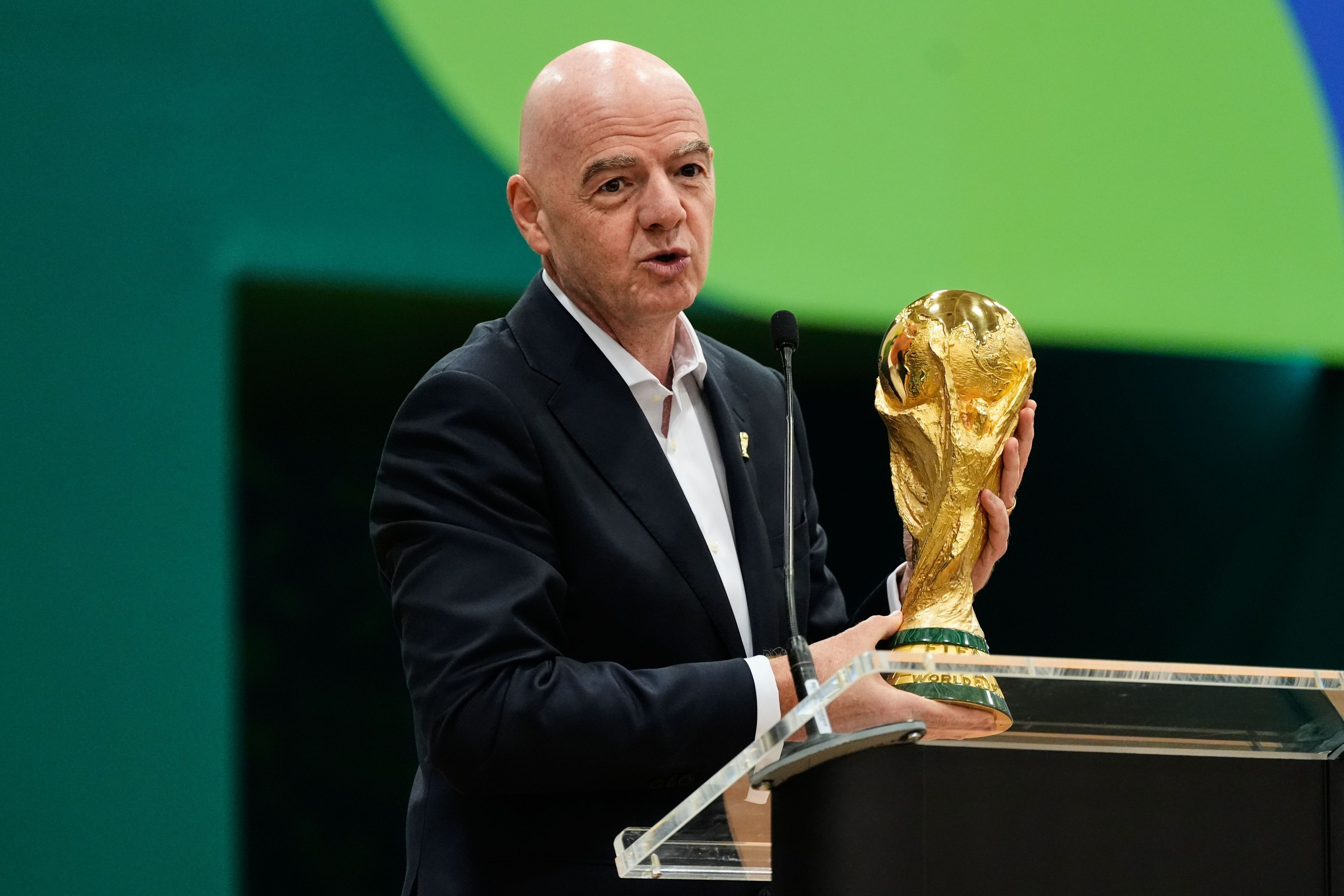 Gianni Infantino hält an einem Rednerpult den WM-Pokal in den Händen.