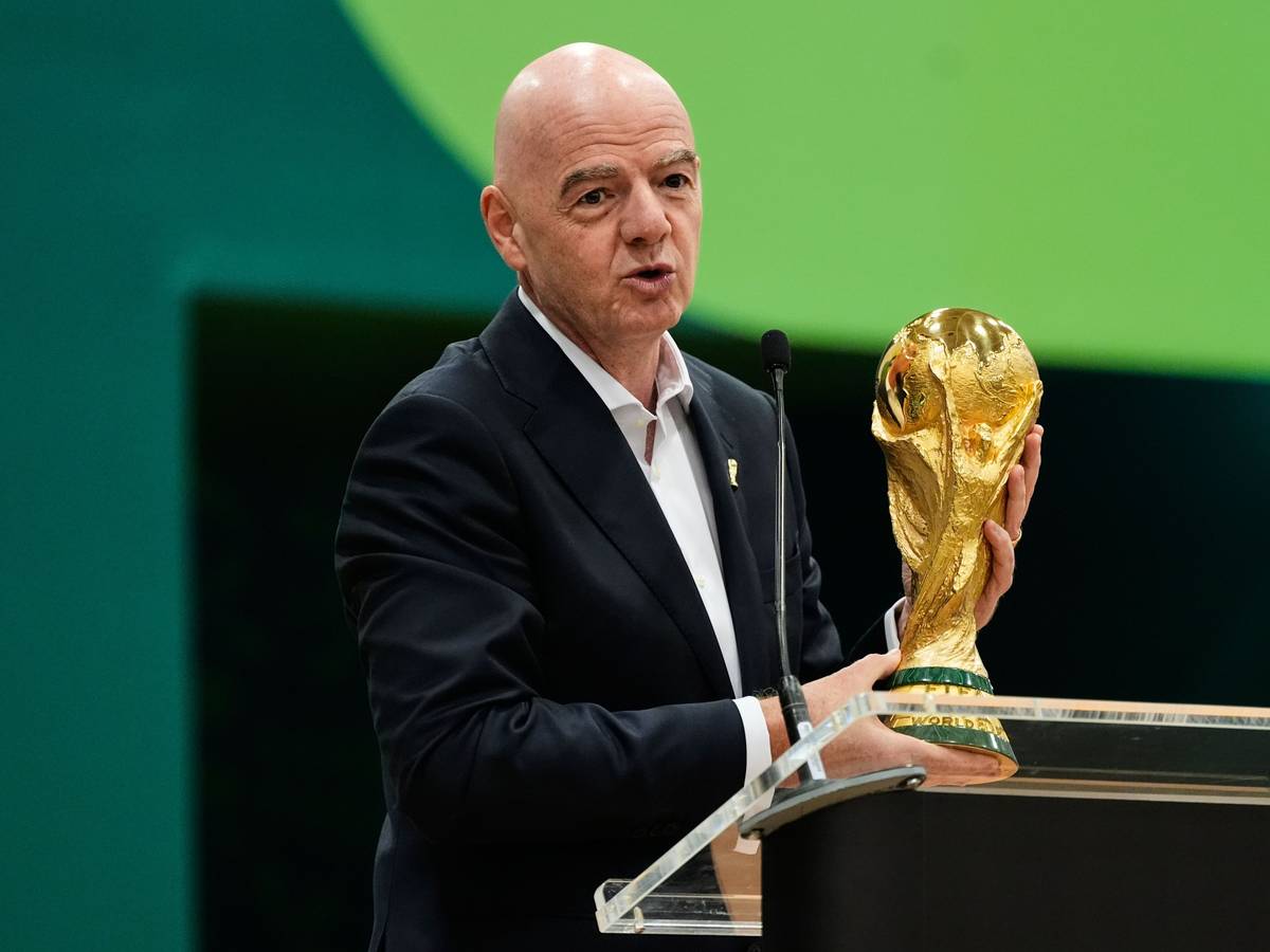 Gianni Infantino hält an einem Rednerpult den WM-Pokal in den Händen.