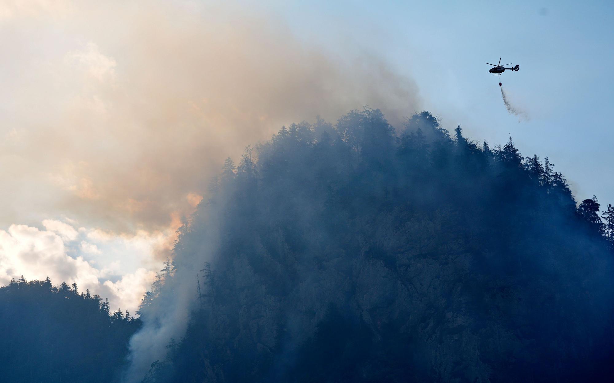 Ein Hubschrauber lässt zur Bekämpfung eines Brandes im Bergwald in den Chiemgauer Alpen Löschwasser ab.