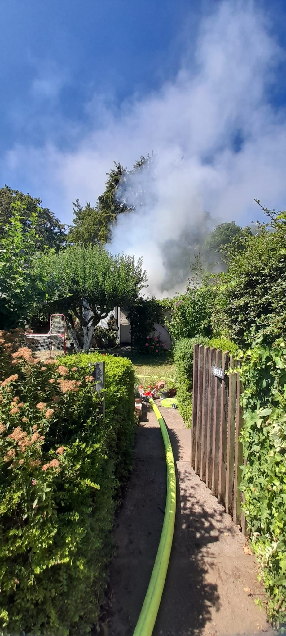 Von einem Garten aus ist aufsteigender Brandrauch zu sehen.