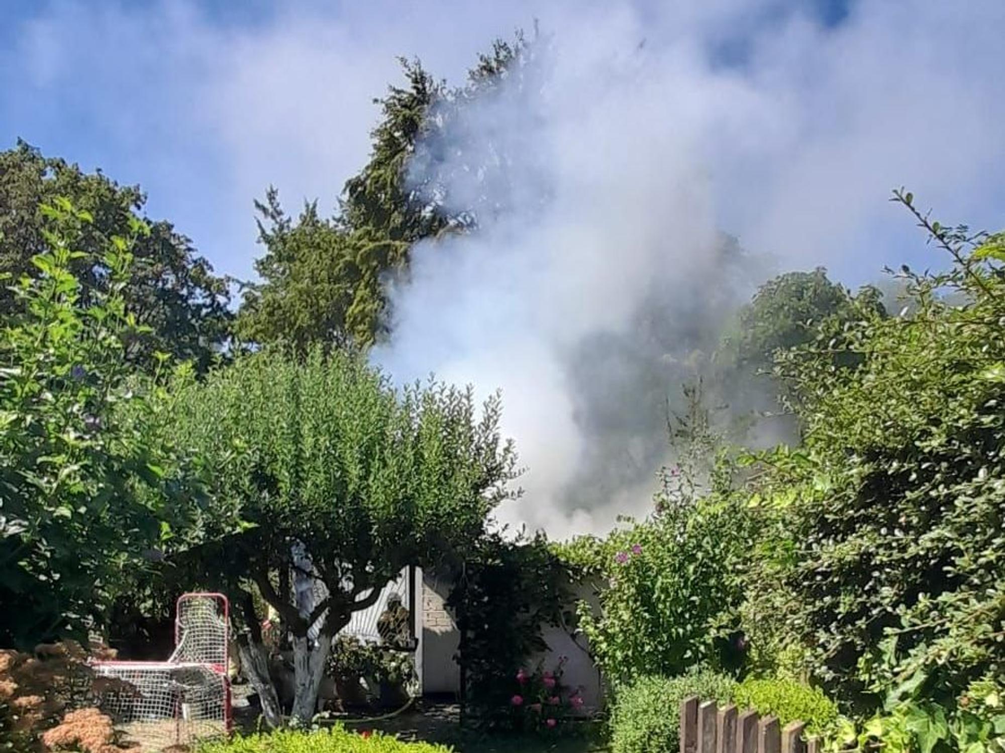 Von einem Garten aus ist aufsteigender Brandrauch zu sehen.