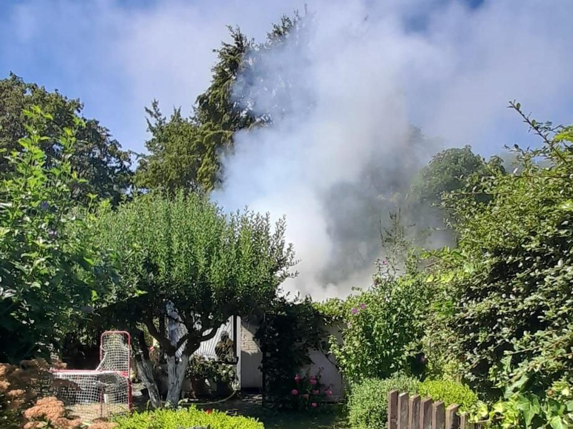 Von einem Garten aus ist aufsteigender Brandrauch zu sehen.