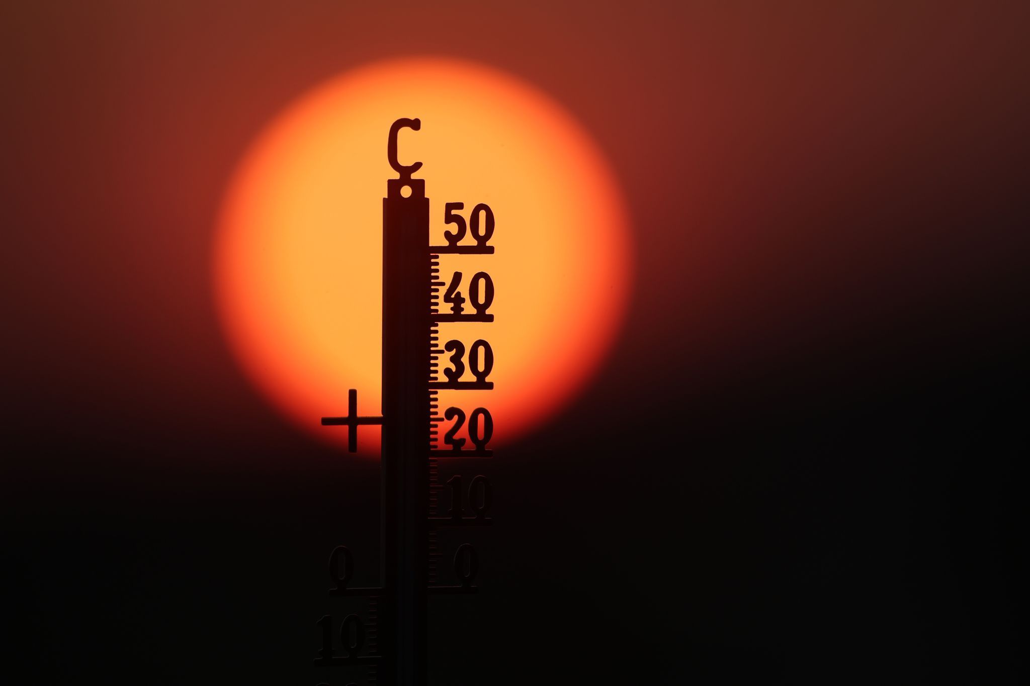 Hitze in Deutschland: Ein Thermometer vor einer rotglühenden Sonne