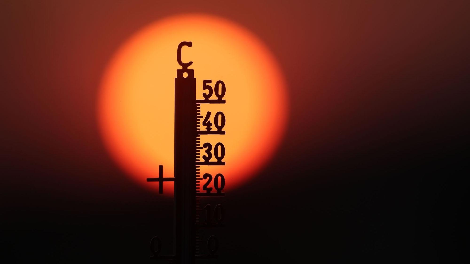 Hitze in Deutschland: Ein Thermometer vor einer rotglühenden Sonne