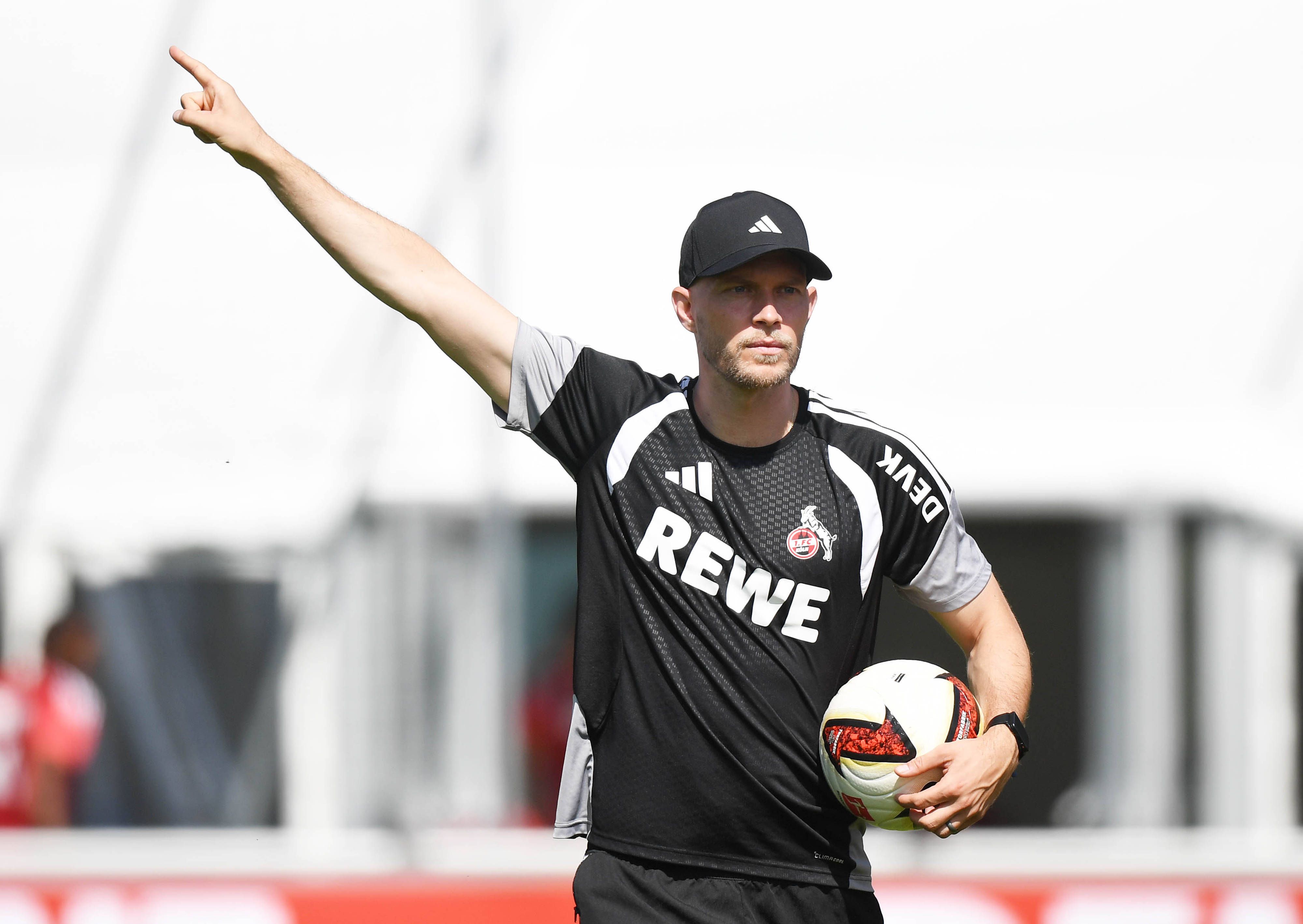 René Wagner hat einen Ball in der Hand und zeigt mit der anderen mit ausgestrecktem Zeigefinger nach oben.