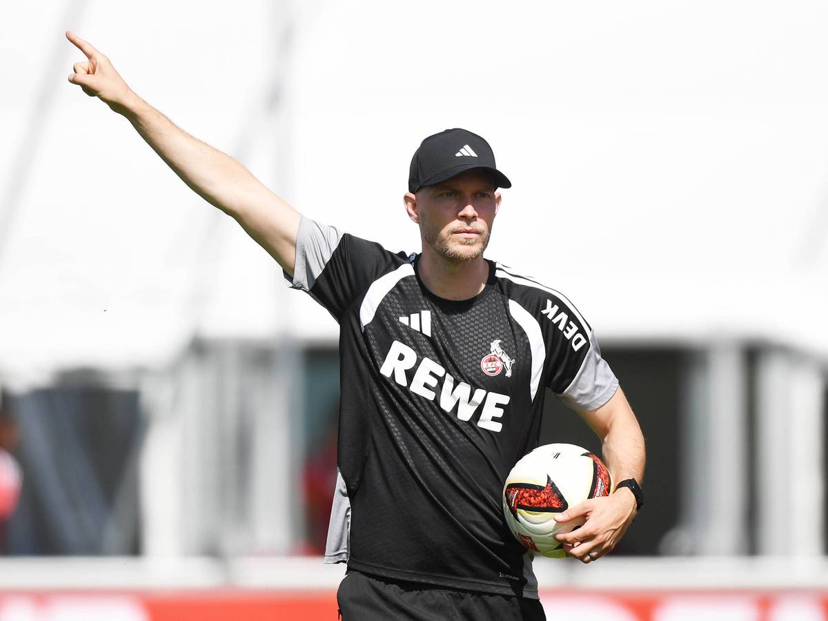 René Wagner hat einen Ball in der Hand und zeigt mit der anderen mit ausgestrecktem Zeigefinger nach oben.