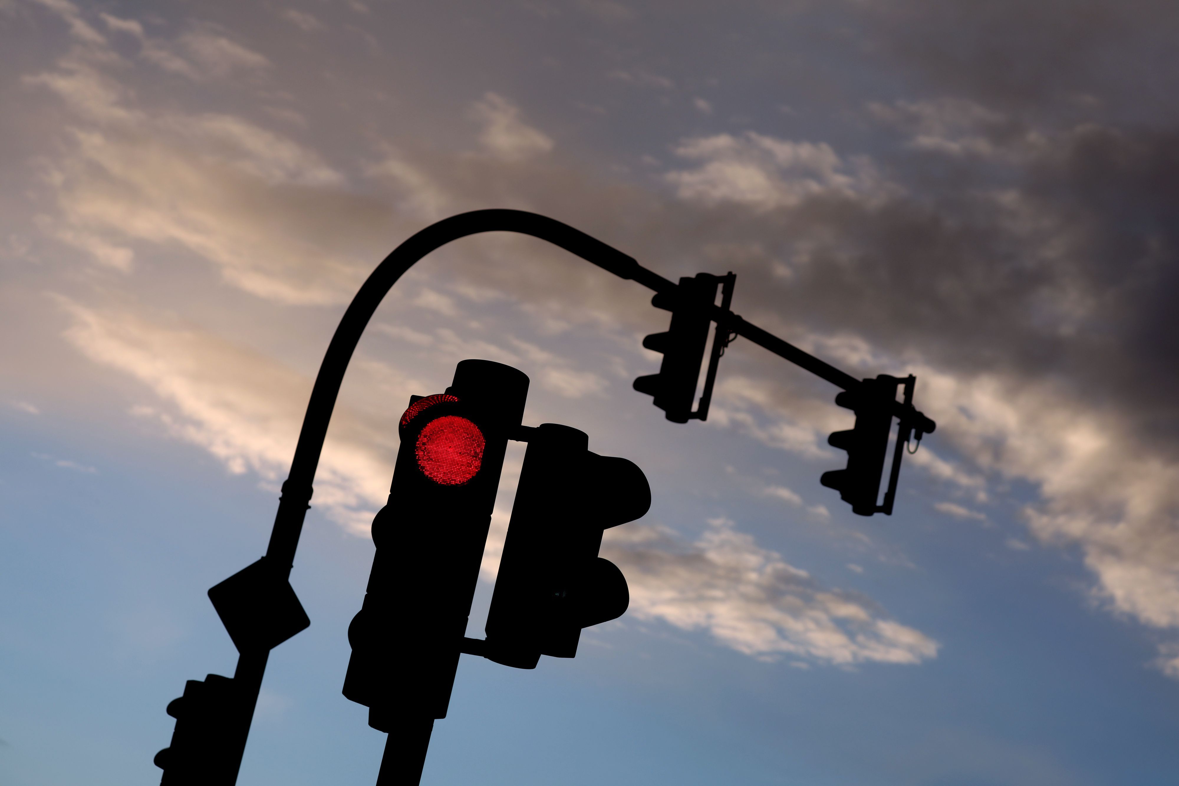 Eine auf Rot stehende Ampel leuchtet am frühen Morgen vor teilweise bewölktem Himmel. (Symbolfoto)