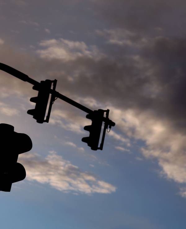 Eine auf Rot stehende Ampel leuchtet am frühen Morgen vor teilweise bewölktem Himmel. (Symbolfoto)