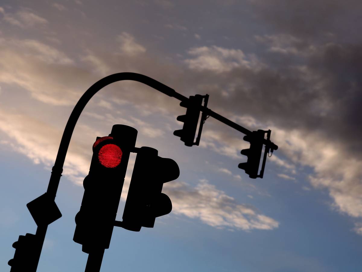 Eine auf Rot stehende Ampel leuchtet am frühen Morgen vor teilweise bewölktem Himmel. (Symbolfoto)