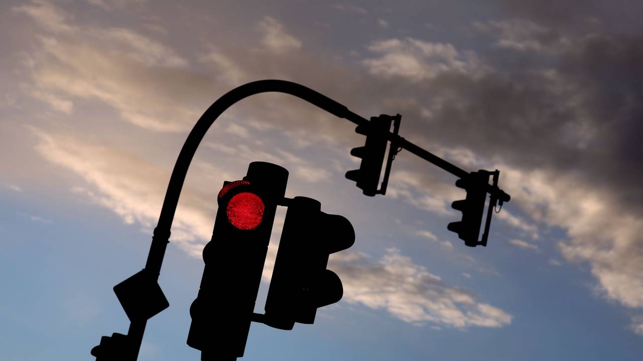 Eine auf Rot stehende Ampel leuchtet am frühen Morgen vor teilweise bewölktem Himmel. (Symbolfoto)