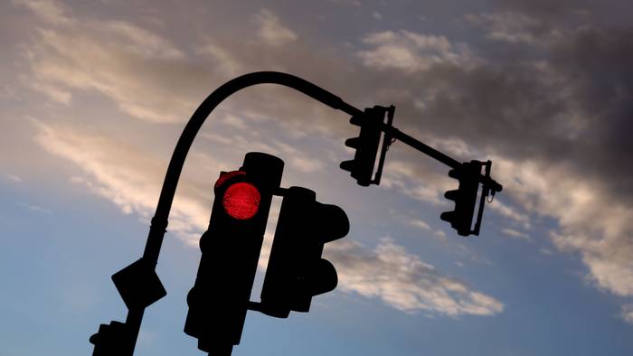 Eine auf Rot stehende Ampel leuchtet am frühen Morgen vor teilweise bewölktem Himmel. (Symbolfoto)