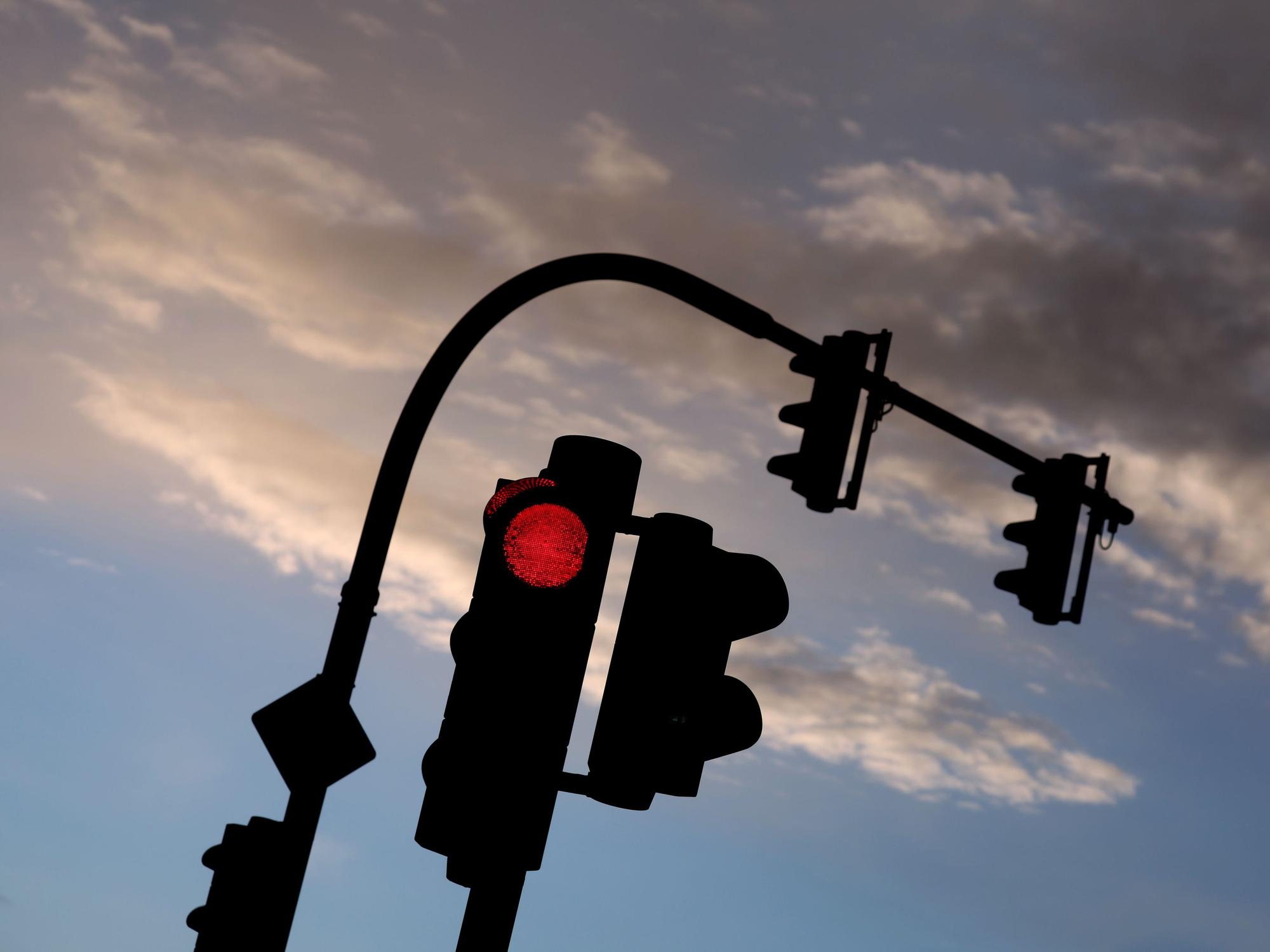 Eine auf Rot stehende Ampel leuchtet am frühen Morgen vor teilweise bewölktem Himmel. (Symbolfoto)