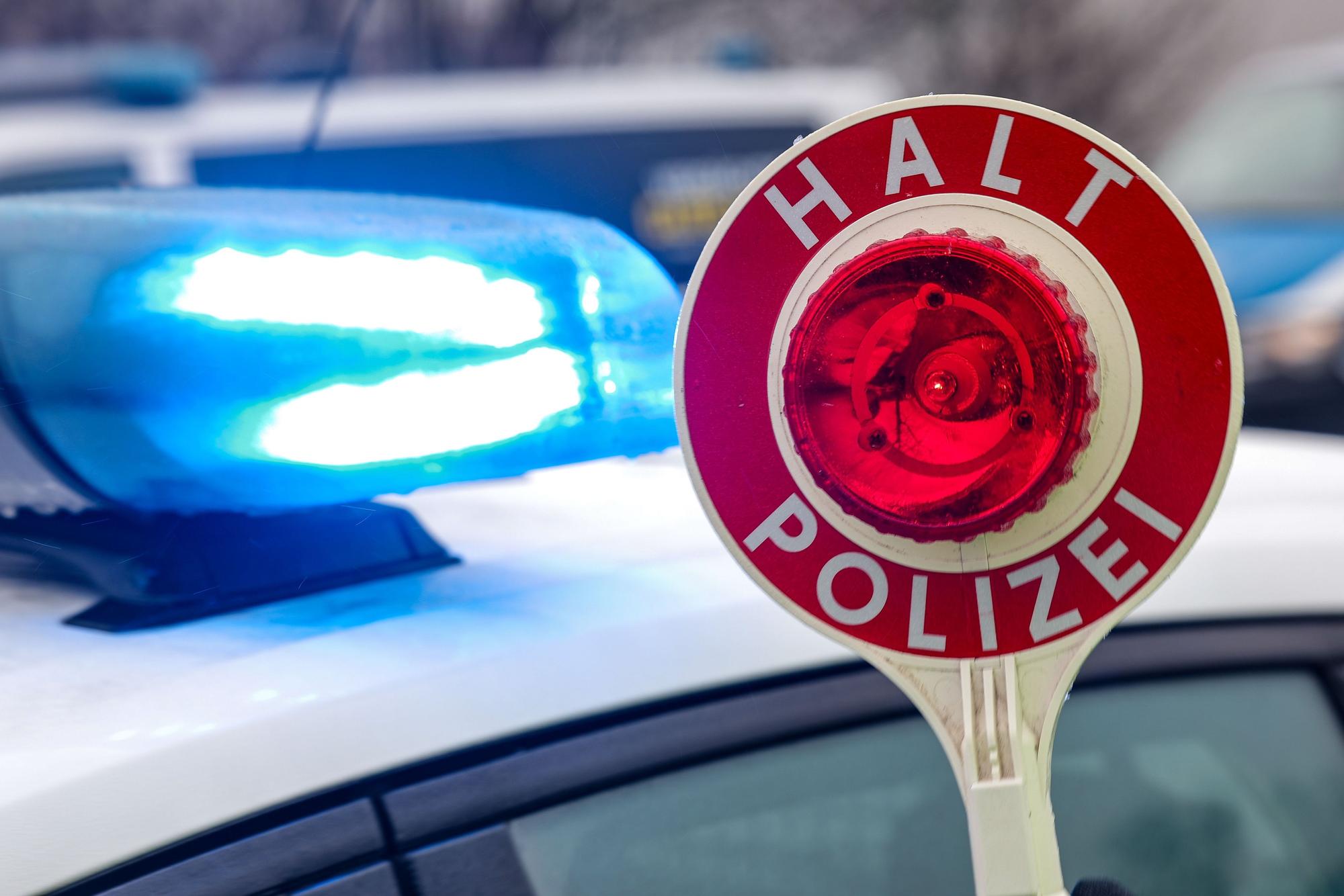 Polizei-Kelle mit Polizei-Auto im Hintergrund.