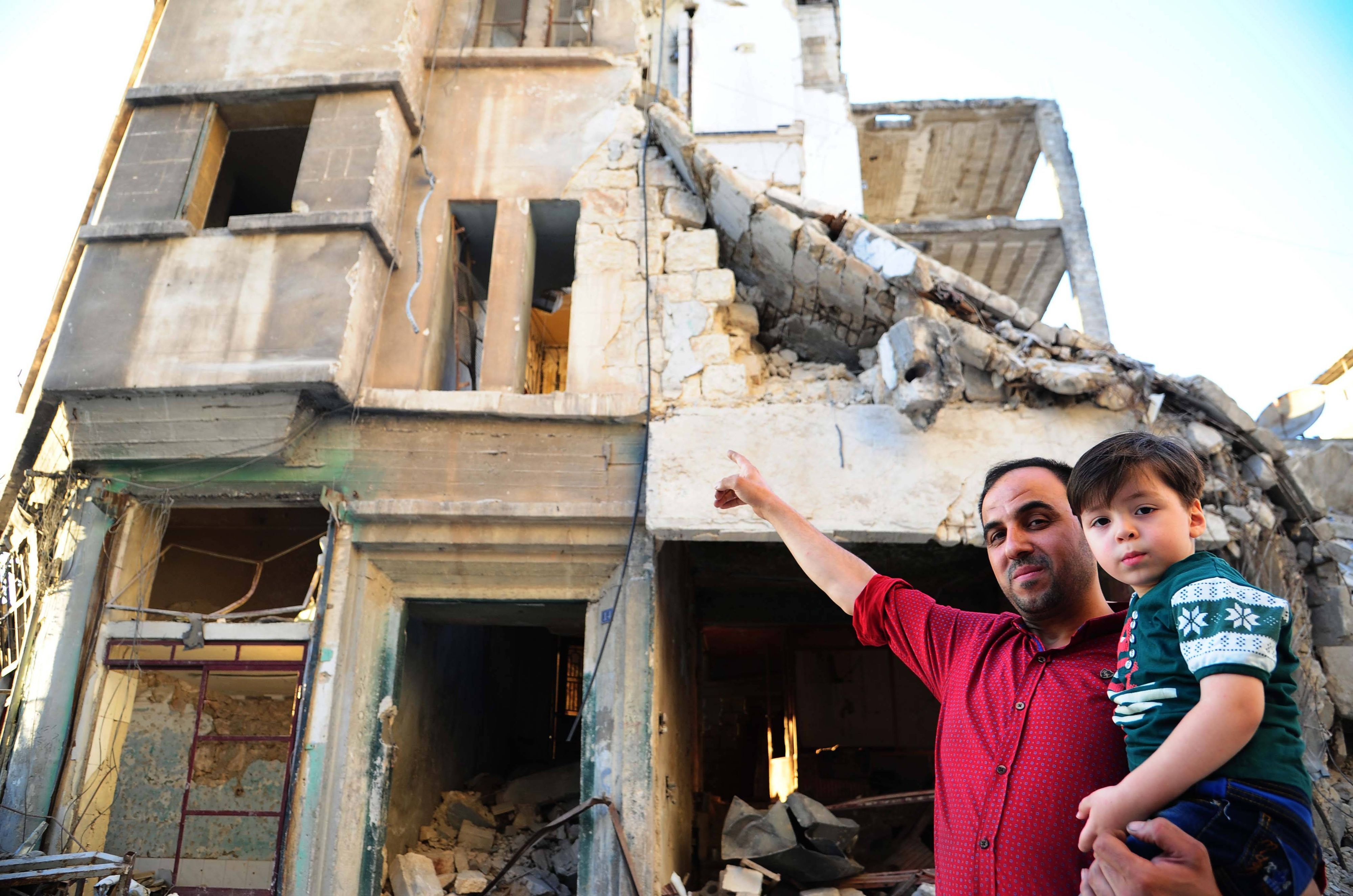 Omran Daqneesh (rechts) mit seinem Vater vor ihrem teilweise zerstörten Haus im Stadtteil Karm al-Qaterji in Aleppo. Das Foto entstand 2017, ein Jahr nachdem die Aufnahme des Jungen im Krankenwagen weltweit bekannt geworden war.