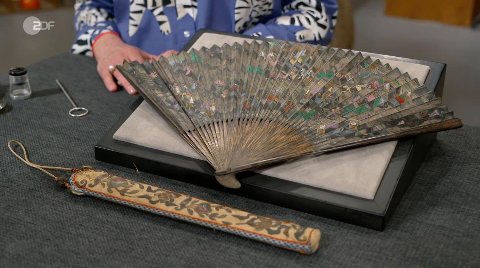 Als weiteres Objekt der Sendung wurde ein chinesischer, handbemalter Fächer aus geflochtenem Papier und Bambus von Friederike Werner zwischen 1906 und 1926 datiert. Sie schätzte den Wert auf 300 Euro - ähnlich wie der Wunschpreis von 200 bis 300 Euro. Sarah Schreiber zahlte für den „wunderschönen Fächer“ sogar 600 Euro. (Bild: ZDF)
