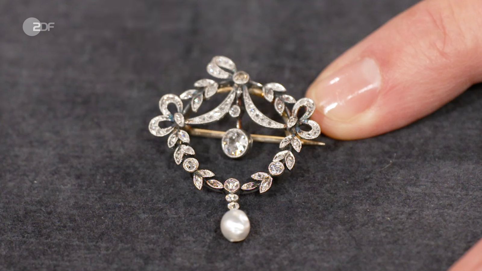 Eine Jugendstil-Brosche aus dem Familienbesitz datierte Heide Rezepa-Zabel auf 1900 bis 1910. Nach dem Wunschpreis von 1.000 Euro, schätzte sie das Schmuckstück aus Platin und 585er Gold mit Diamanten und Naturperle auf 800 bis 1.000 Euro. Im Händlerraum sicherte sich Sarah Schreiber die Brosche schließlich für 700 Euro. (Bild: ZDF)