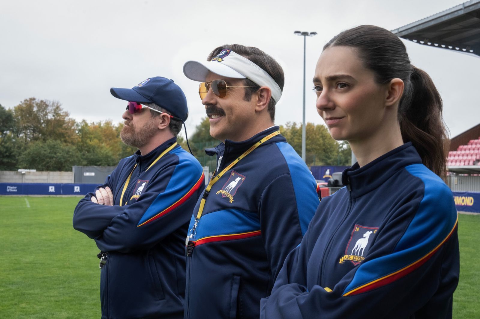 Mit Coach Beard (Brendan Hunt) und der schroffen Alice Chilton (Tanya Reynolds) hat Ted Lasso (Jason Sudeikis, Mitte) zwei hervorragende Co-Trainer an seiner Seite. (Bild: © Apple TV / Collin Hutton)