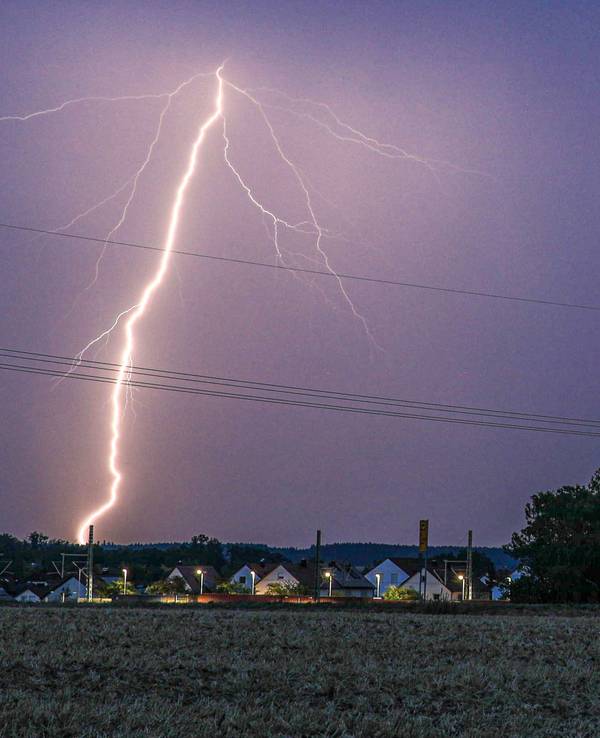 Ein Blitz erhellt bei einem abendlichen Sommergewitter den Himmel.