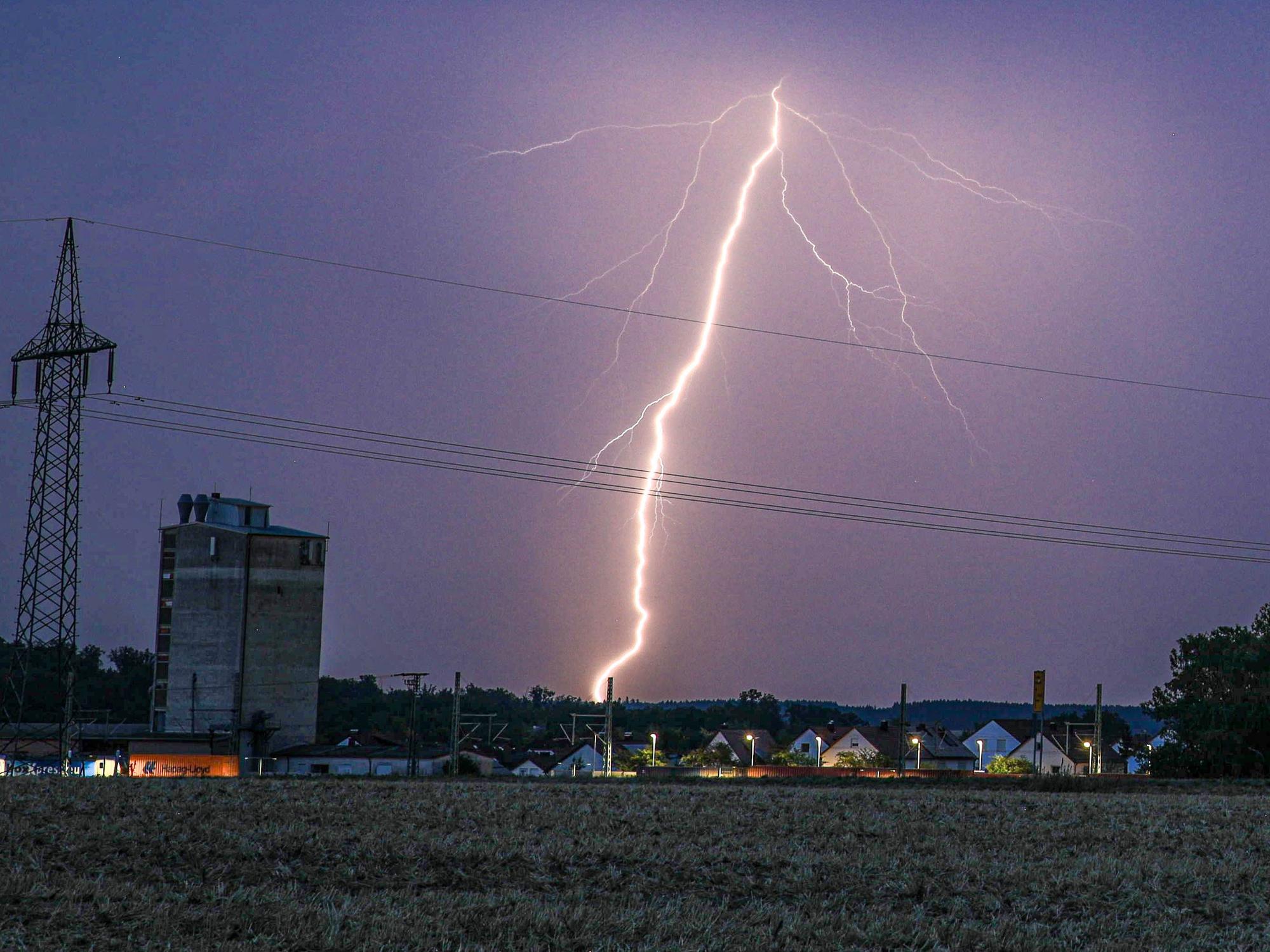 Ein Blitz erhellt bei einem abendlichen Sommergewitter den Himmel.