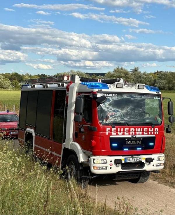 Auf einem unbefestigten Weg stehen Feuerwehrfahrzeuge, nebenan auf einem Feld ist ein Hubschrauber gelandet.