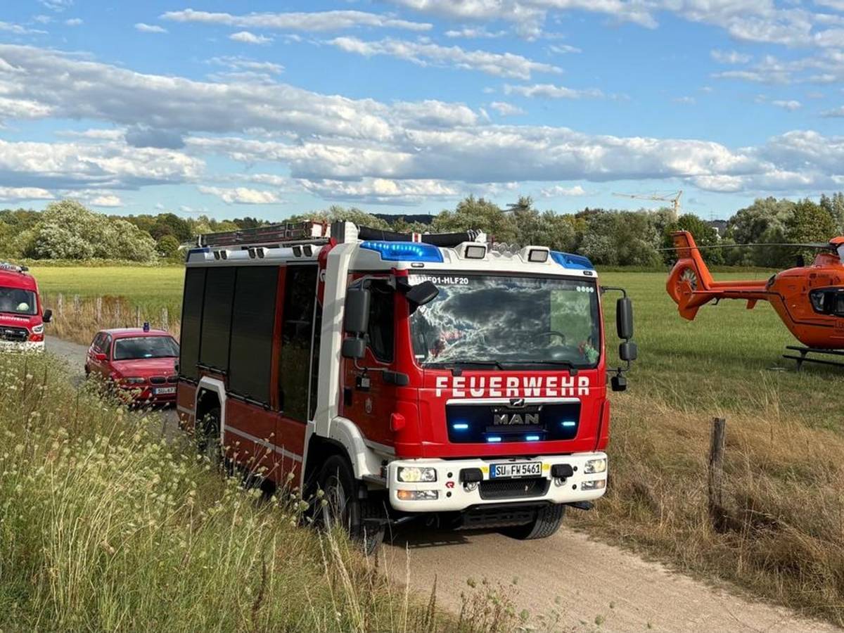 Auf einem unbefestigten Weg stehen Feuerwehrfahrzeuge, nebenan auf einem Feld ist ein Hubschrauber gelandet.