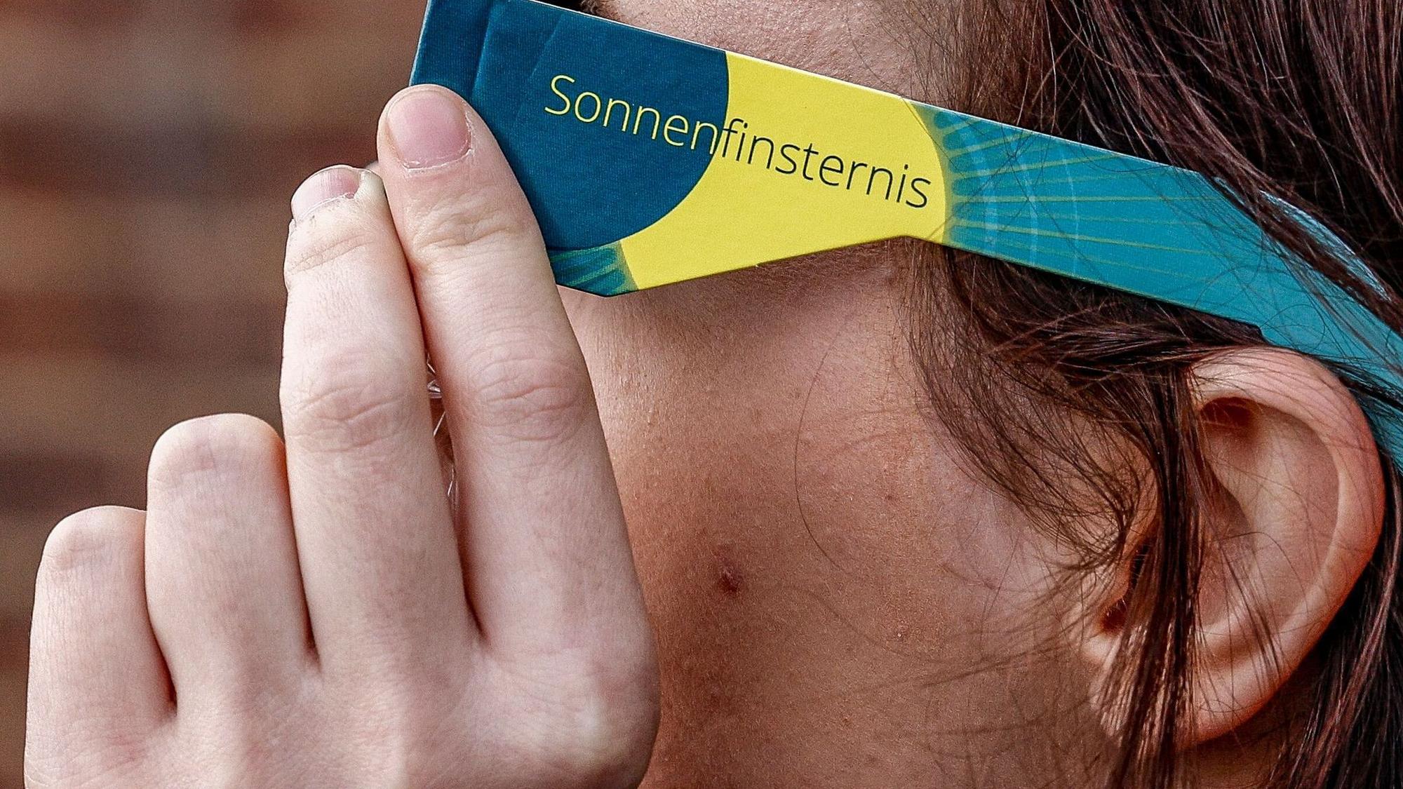 Frau mit Schutzbrille betrachtet eine partielle Sonnenfinsternis