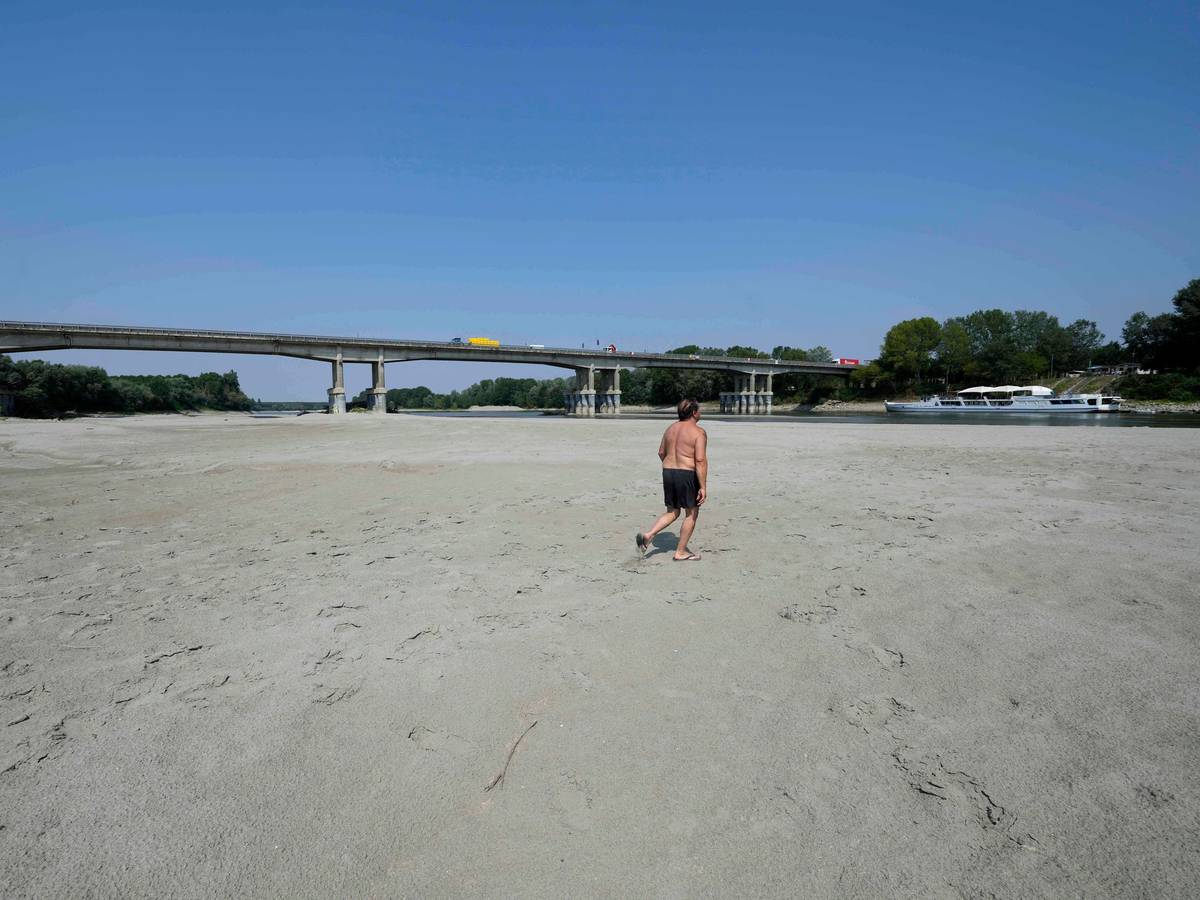 Mann geht in ausgetrocknetem Flussbett unter Brücke