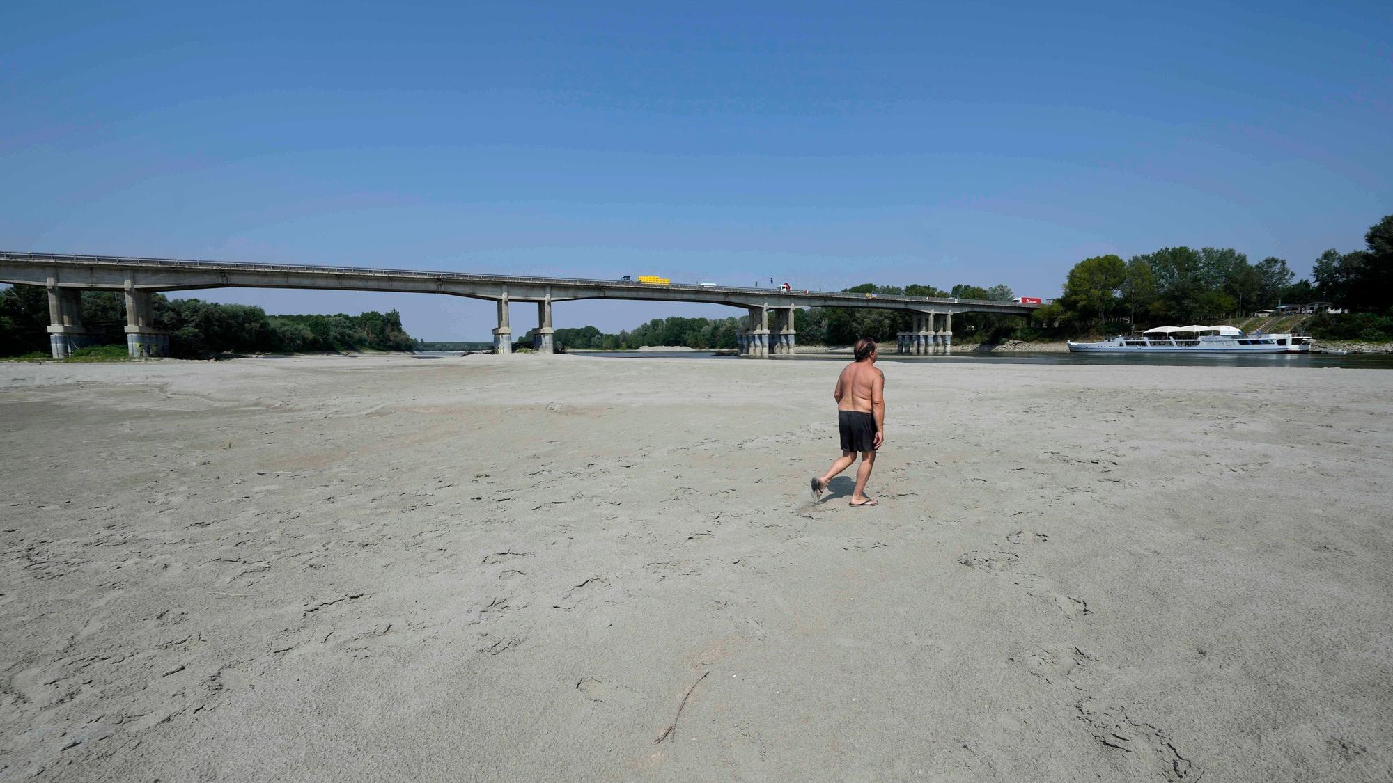 Mann geht in ausgetrocknetem Flussbett unter Brücke
