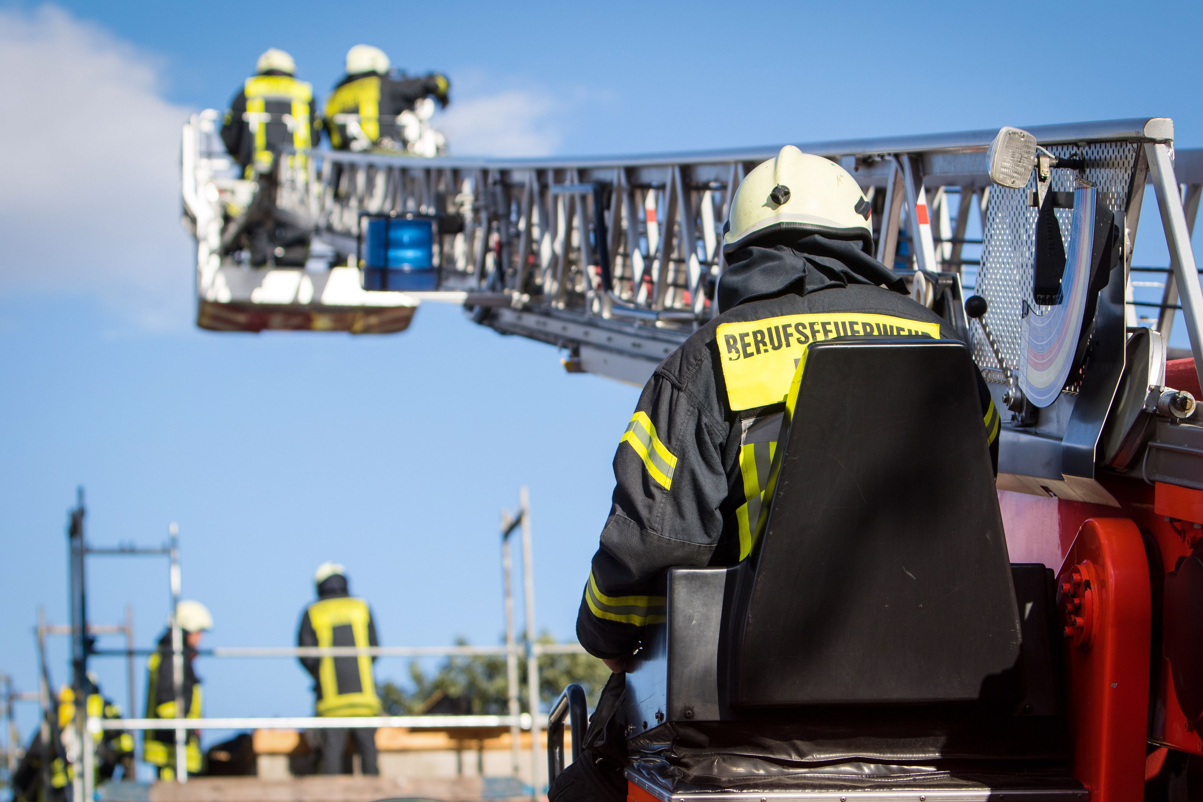 Zwei Feuerwehrleute stehen im Korb der Drehleiter, die auf ein Gebäude ragt.