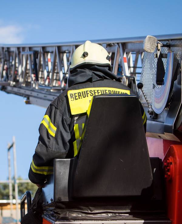 Zwei Feuerwehrleute stehen im Korb der Drehleiter, die auf ein Gebäude ragt.