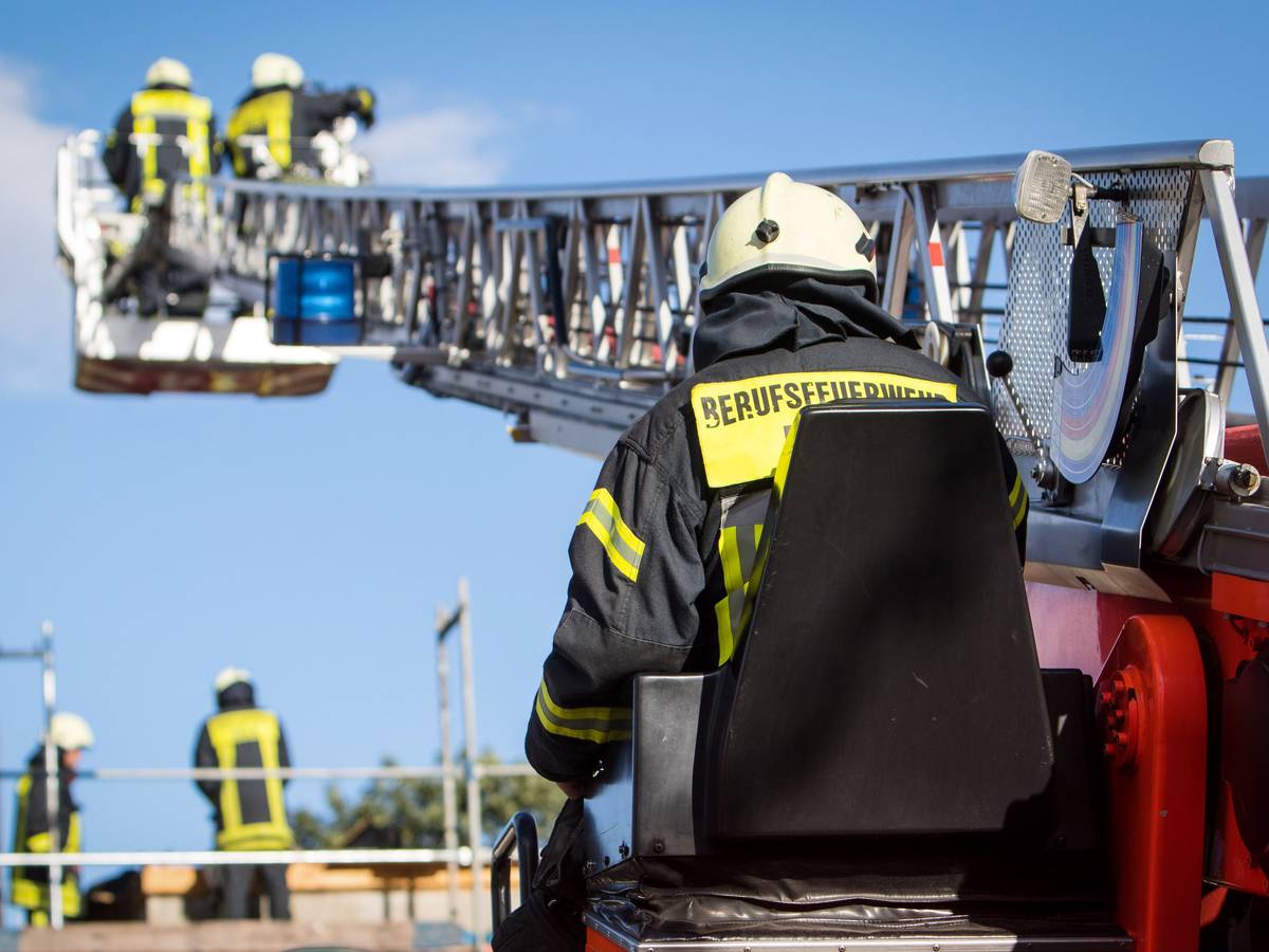 Zwei Feuerwehrleute stehen im Korb der Drehleiter, die auf ein Gebäude ragt.