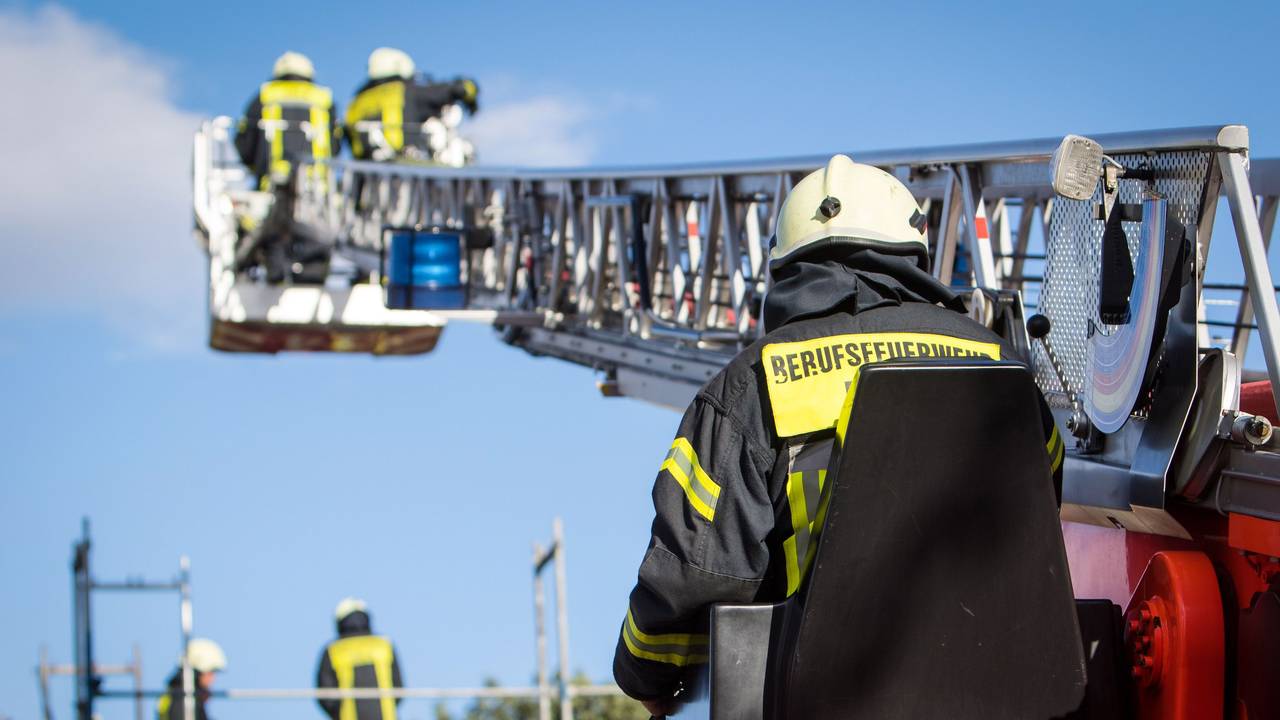Zwei Feuerwehrleute stehen im Korb der Drehleiter, die auf ein Gebäude ragt.