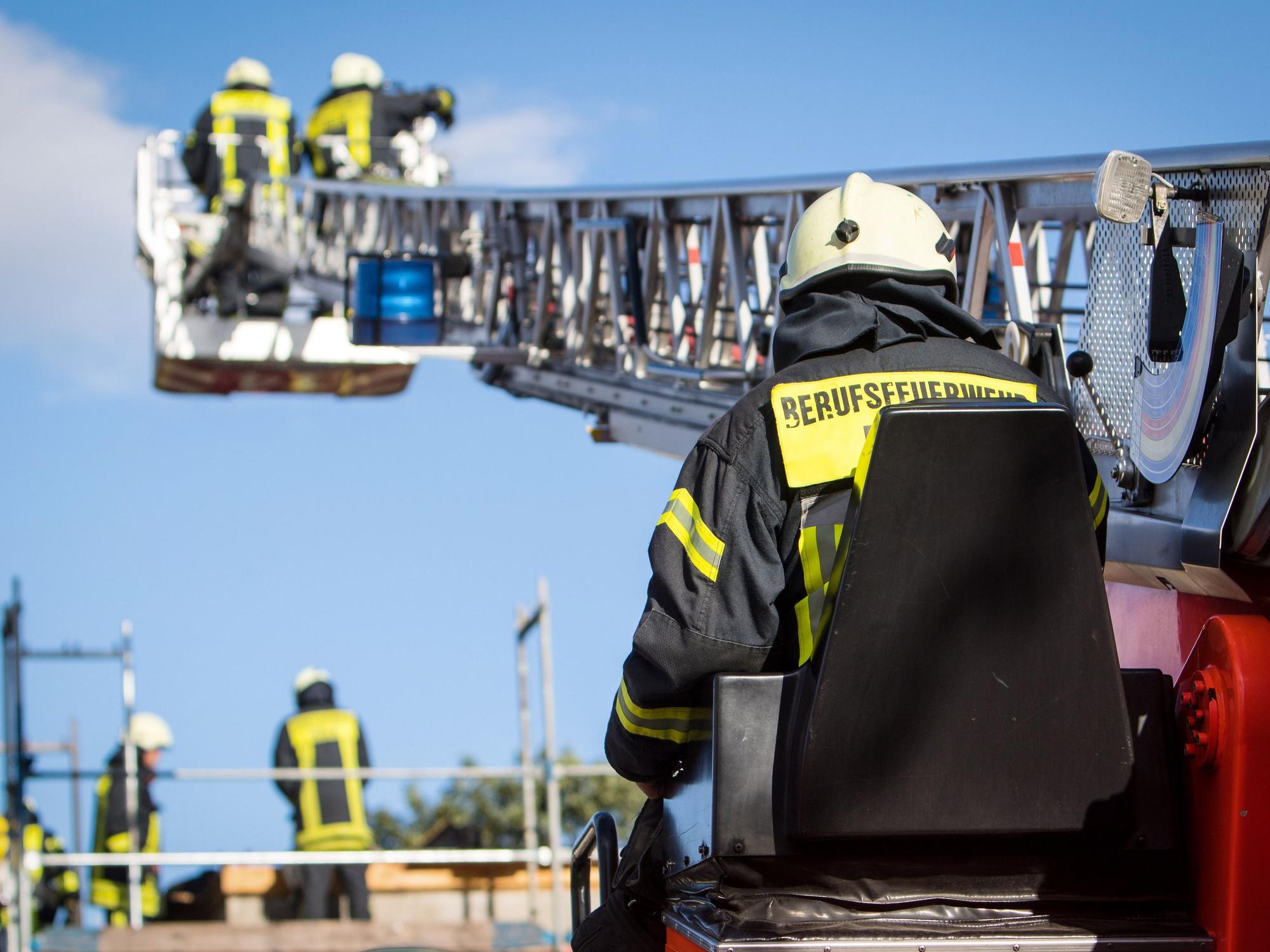 Zwei Feuerwehrleute stehen im Korb der Drehleiter, die auf ein Gebäude ragt.