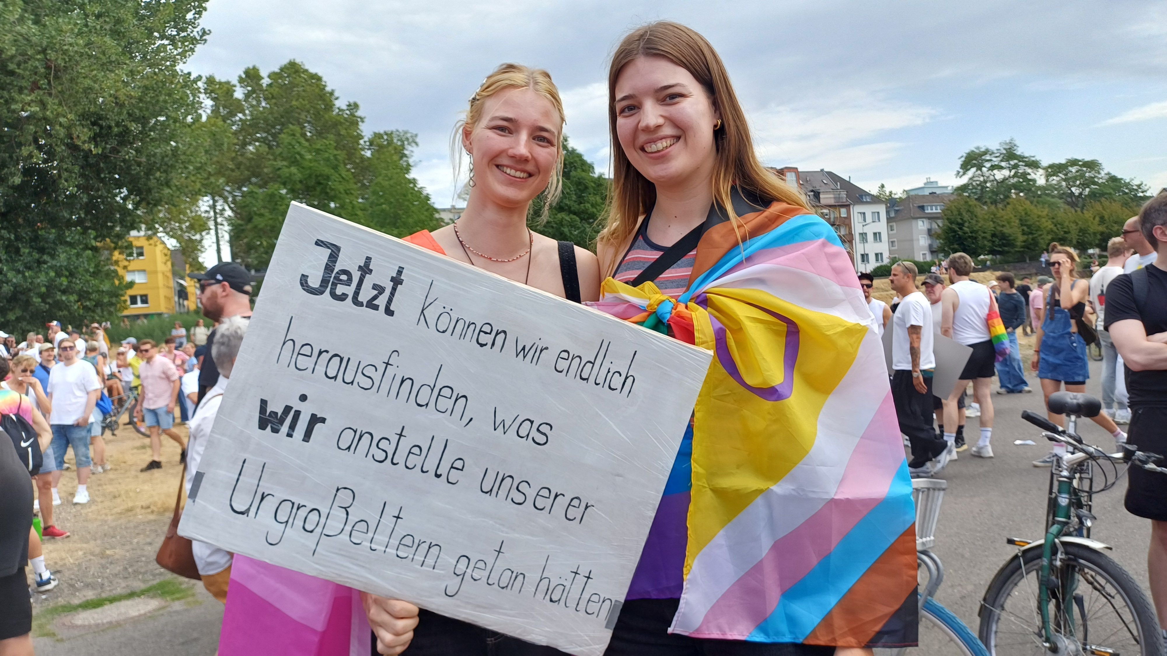Zwei junge Frauen halten ein Plakat mit der Aufschrift: Jetzt können wir endlich herausfinden, was wir anstelle unserer Urgroßeltern getan hätten.