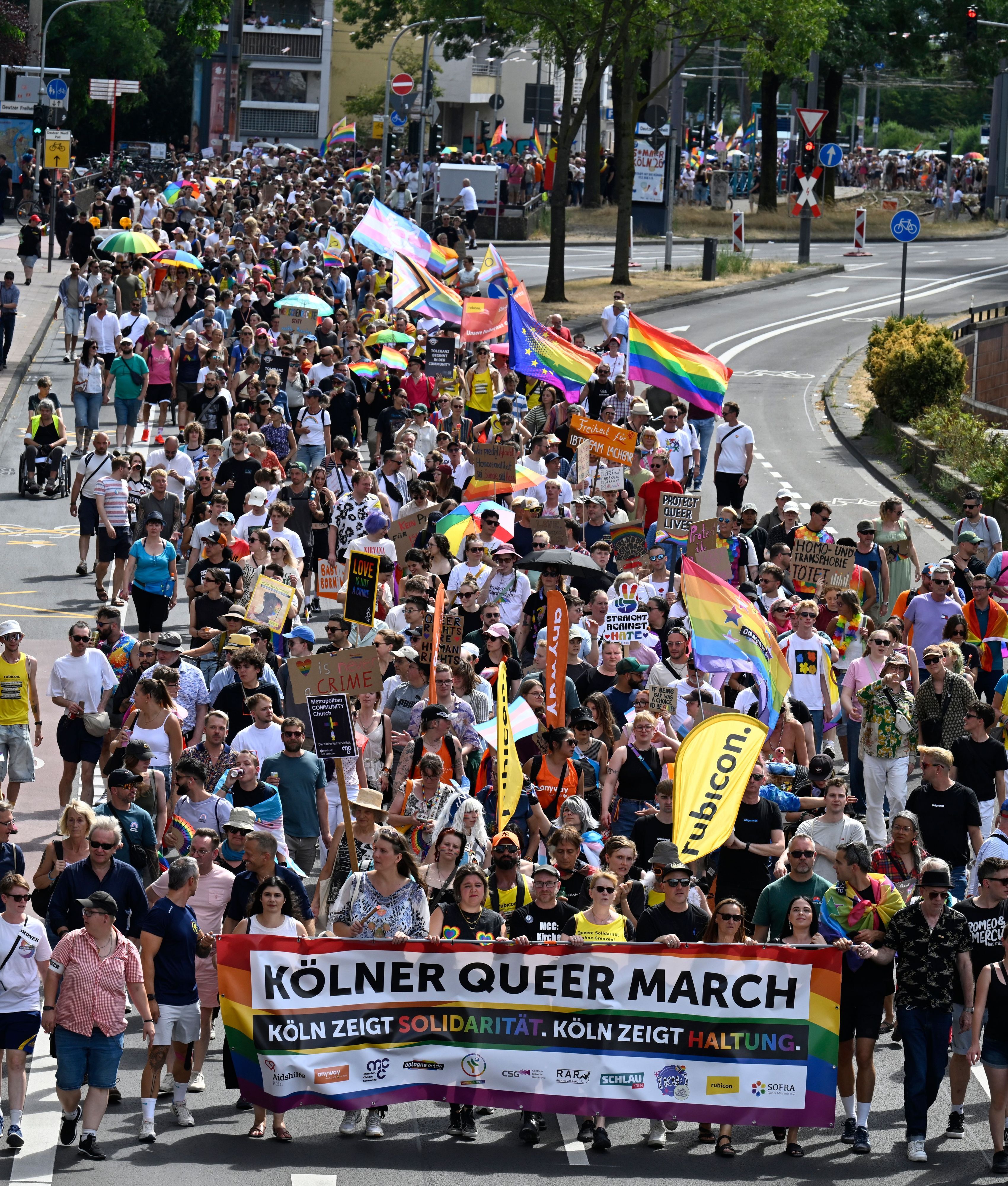 Menschen ziehen über eine Straße, die vorderen halten ein Transparent mit der Aufschrift: Kölner Queer March, Köln zeigt Solidarität, Köln zeigt Haltung.