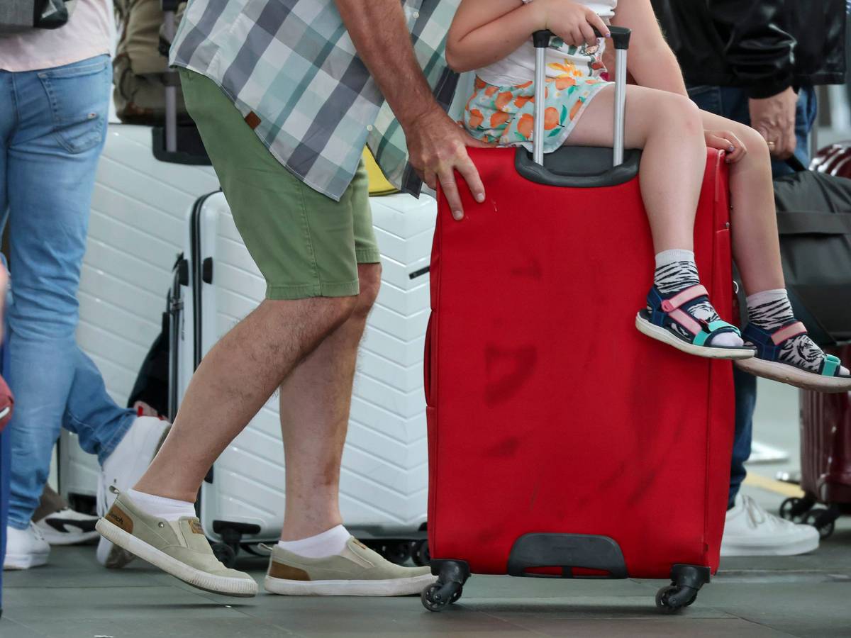 Ein Mann schiebt einen Koffer mit einem Kind zum Check-in. (Symbolfoto)