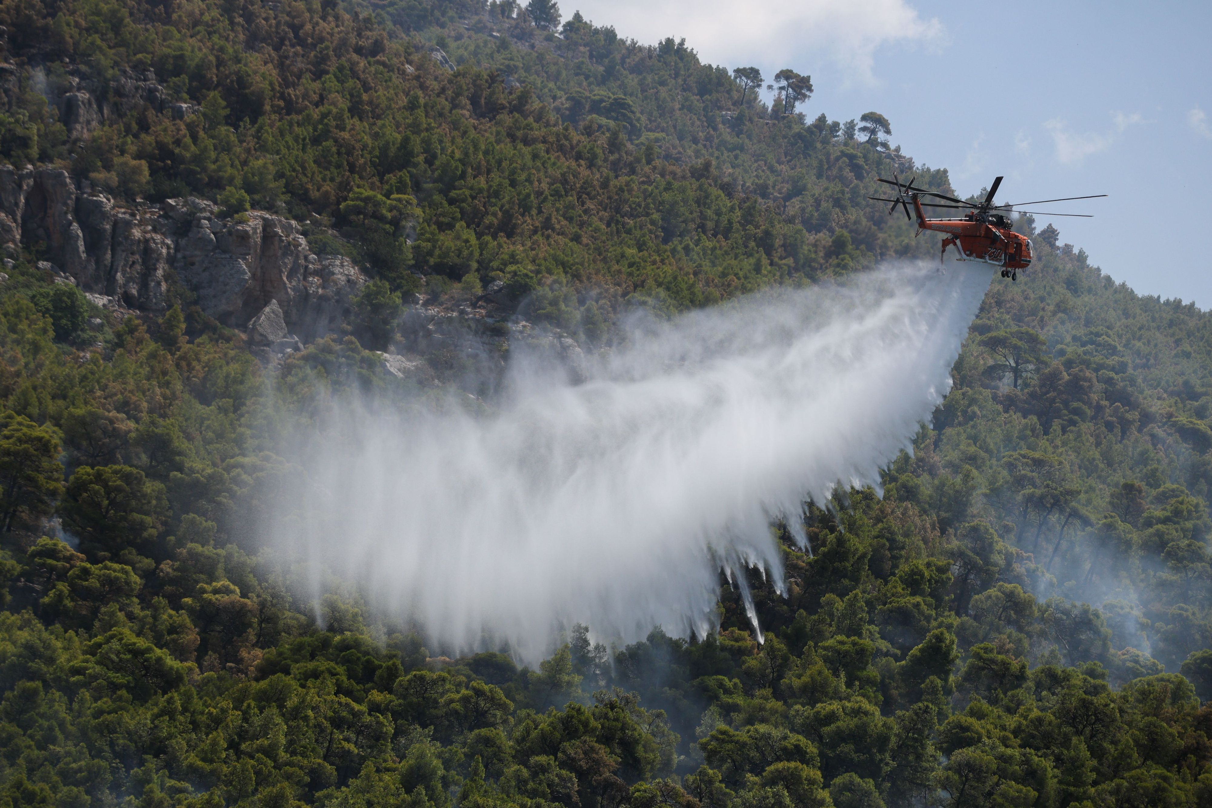 Ein Löschhubschrauber wirft Wasser über einem Wald nahe dem Dorf Loumpa ab.