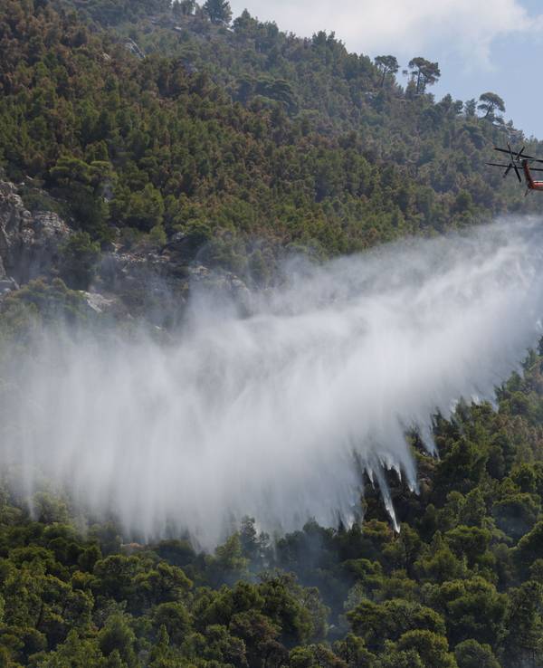 Ein Löschhubschrauber wirft Wasser über einem Wald nahe dem Dorf Loumpa ab.