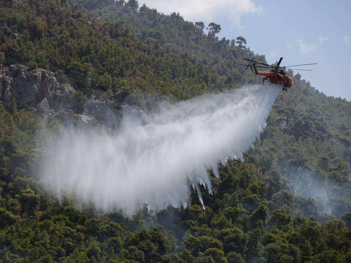 Ein Löschhubschrauber wirft Wasser über einem Wald nahe dem Dorf Loumpa ab.