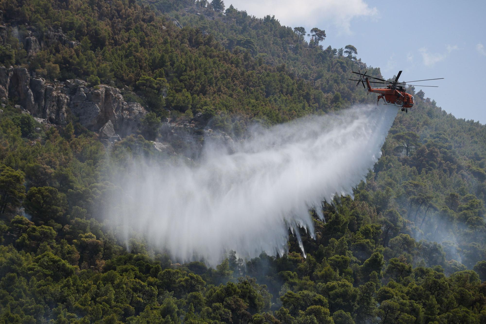Ein Löschhubschrauber wirft Wasser über einem Wald nahe dem Dorf Loumpa ab.
