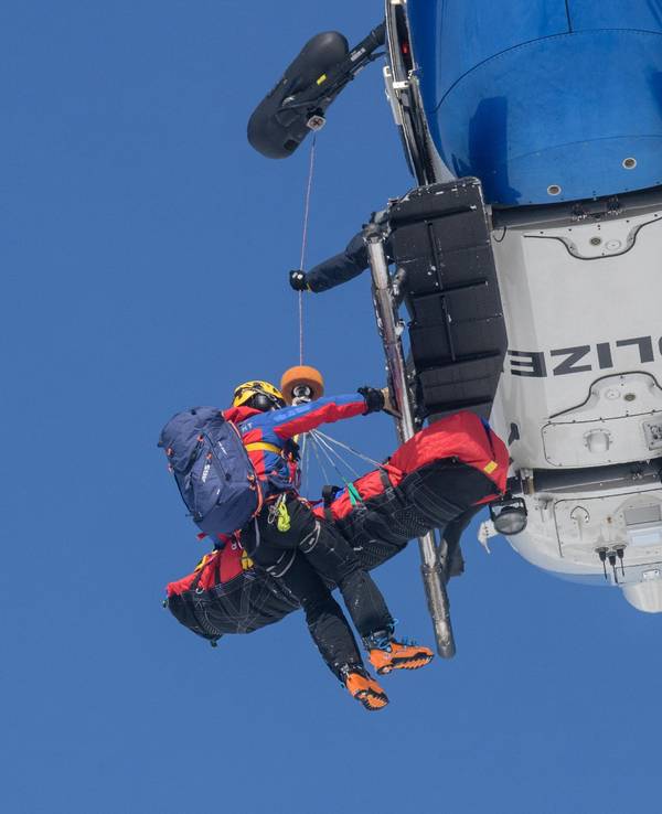 Ein Bergwachtmann und eine geretteten Person werden in einen Polizeihubschrauber gezogen.