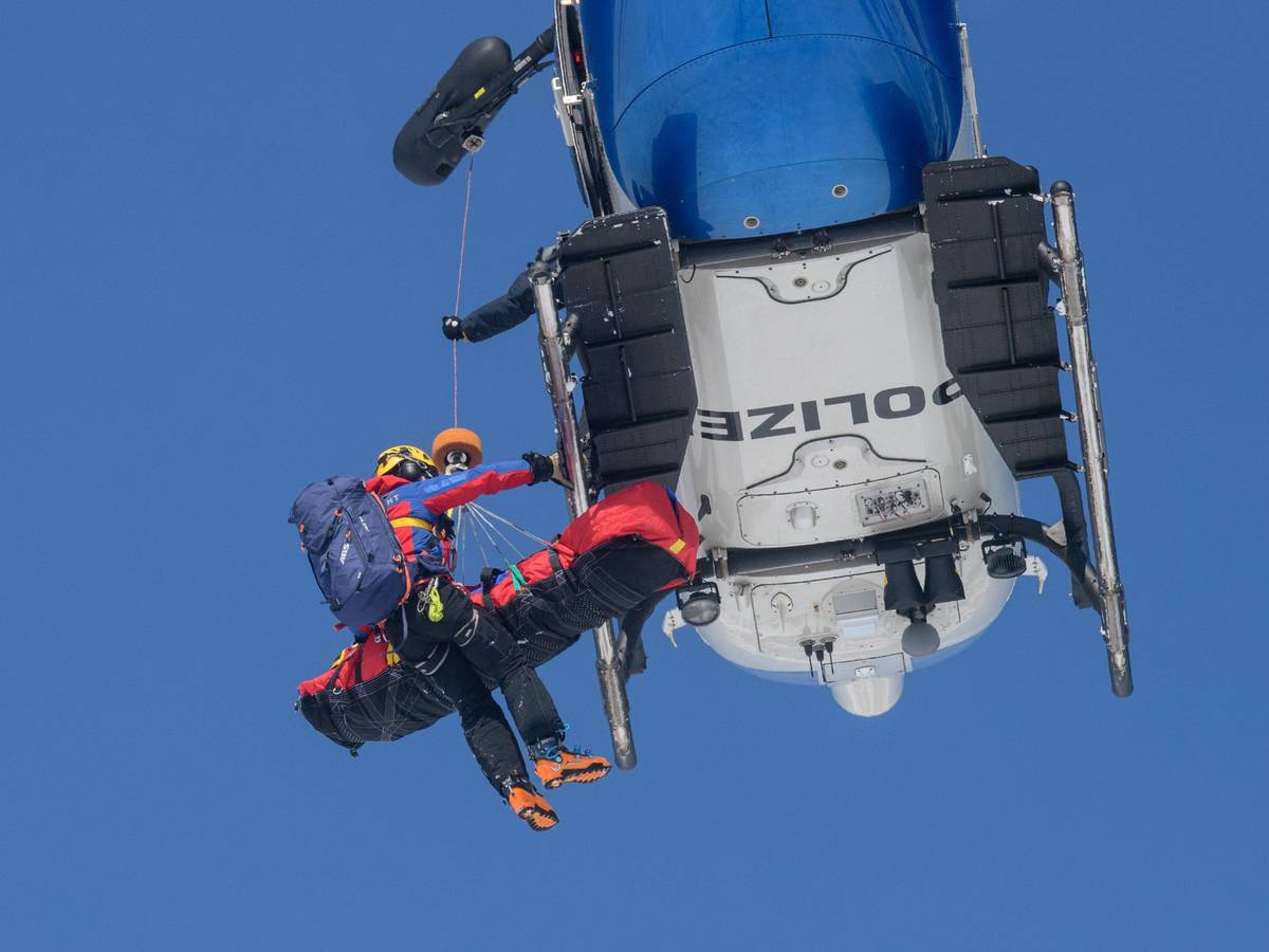 Ein Bergwachtmann und eine geretteten Person werden in einen Polizeihubschrauber gezogen.
