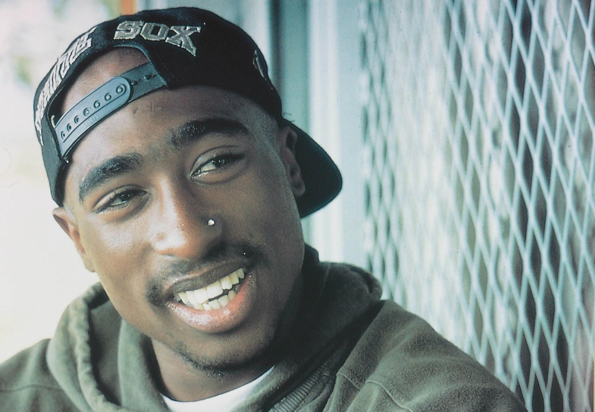 Tupac Shakur posiert und lächelt.