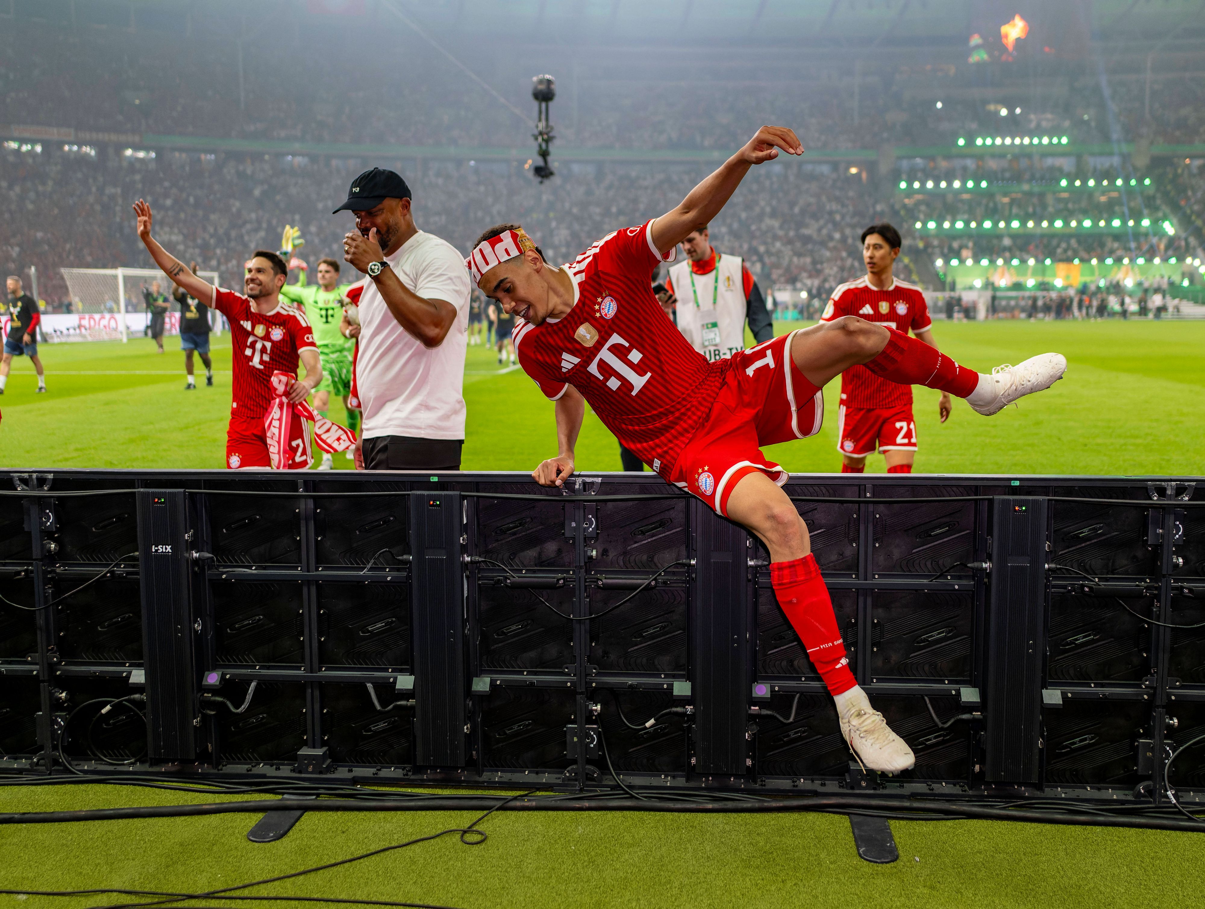 Bayerns Jamal Musiala klettert nach dem Pokalsieg über die Bande im Olympiastadion.